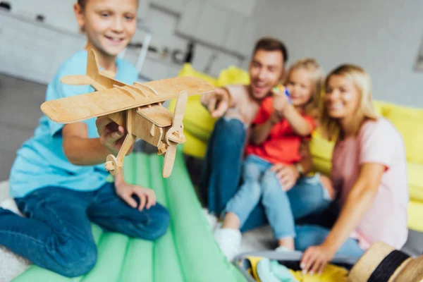 Boy playing with toy wooden airplane with family having fun on background — Stock Photo