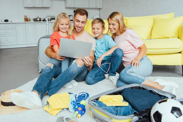 Familia feliz usando el ordenador portátil, planeando vacaciones de verano, embalaje de equipaje y tener un gran tiempo, concepto de viaje - foto de stock