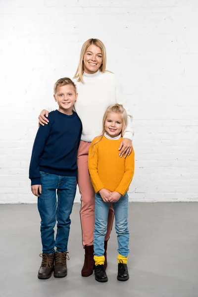 Happy mother hugging son and daughter looking at camera on white background — Stock Photo