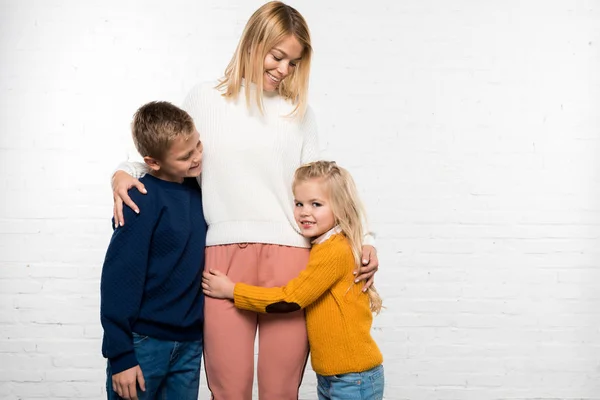 Feliz madre abrazando hijo e hija sobre fondo blanco - foto de stock