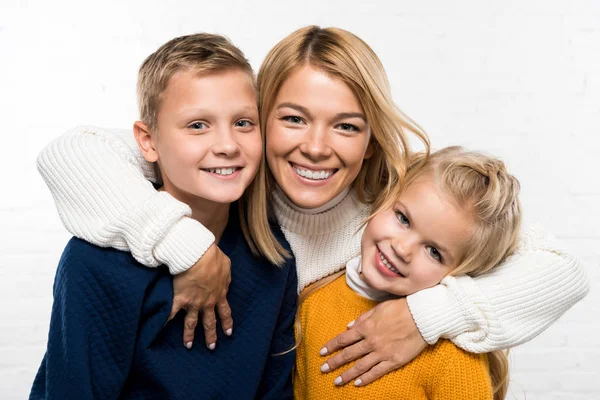 Familienporträt einer glücklichen Mutter, die Sohn und Tochter umarmt und in die Kamera auf weißem Hintergrund blickt — Stockfoto