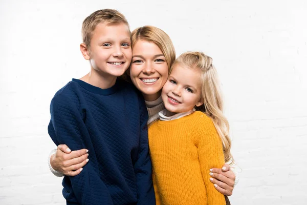 Happy mother hugging son and daughter looking at camera on white background — Stock Photo