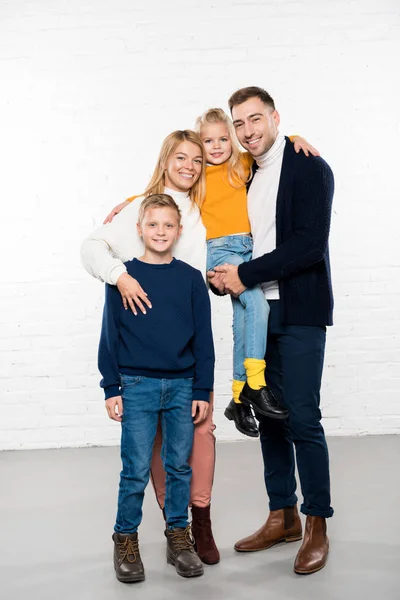 Lächelnde Familie in lässiger Kleidung, die sich umarmt und in die Kamera auf weißem Hintergrund blickt — Stockfoto