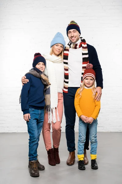 Familia sonriente en ropa de invierno abrazando y mirando a la cámara sobre fondo blanco - foto de stock
