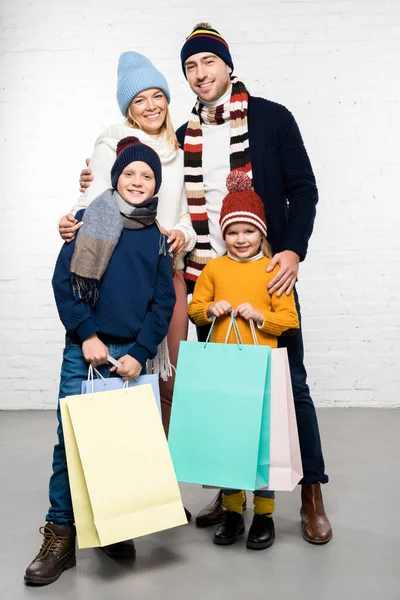 Familia feliz en ropa de invierno mirando a la cámara y sosteniendo bolsas de compras - foto de stock