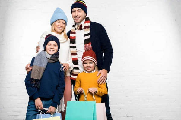 Happy family in winter clothes looking at camera and holding shopping bags — Stock Photo