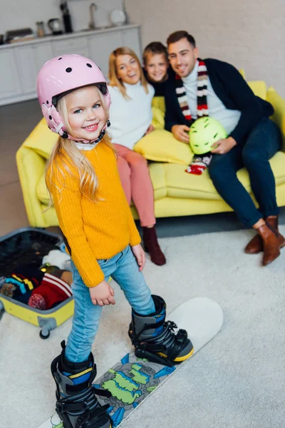 Kind auf Snowboard posiert im Vordergrund, während glückliche Familie viel Spaß hat und für den Winterurlaub einpackt — Stockfoto