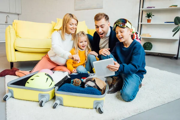 Familia feliz pasar un buen rato, utilizando tableta digital y embalaje para las vacaciones de invierno - foto de stock