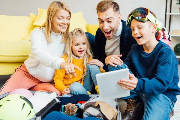 Familia feliz pasar un buen rato, utilizando tableta digital y embalaje para las vacaciones de invierno - foto de stock