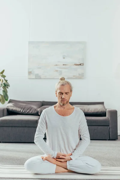 Homem adulto flexível meditando na posição de lótus no tapete de ioga em casa — Fotografia de Stock