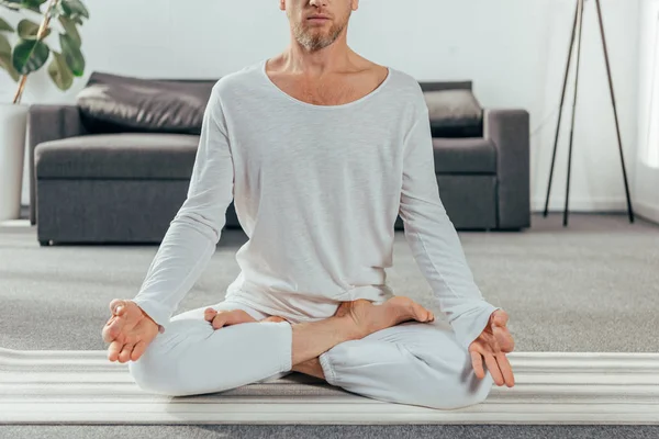 Cropped shot of man in sportswear meditating on yoga mat at home — Stock Photo