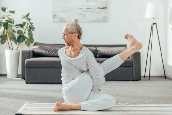 Homme adulte concentré pratiquant le yoga sur tapis à la maison — Photo de stock