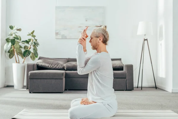 Side view of man sitting in lotus position with mudra sign at home — Stock Photo