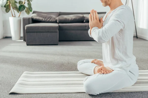 Tiro cortado de homem adulto meditando na posição de lótus no tapete de ioga em casa — Fotografia de Stock