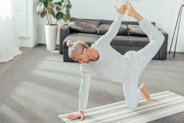 Vista ad alto angolo di esercizio flessibile di yoga uomo adulto sul tappeto a casa — Foto stock