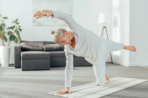 Uomo adulto sportivo in piedi in asana su tappetino yoga a casa — Foto stock