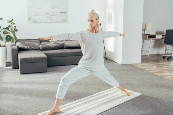 Vista completa del hombre de pie en la postura del yoga del guerrero en la estera en casa - foto de stock