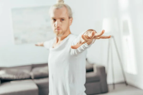 Enfoque selectivo del hombre de pie en la pose de yoga guerrero en casa - foto de stock