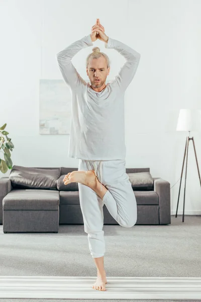 Full length view of man standing in tree pose on yoga mat at home — Stock Photo