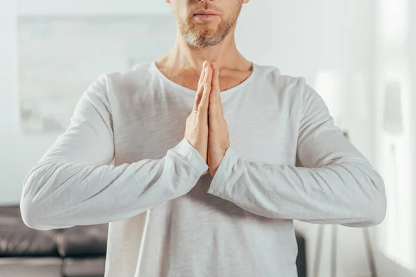 Tiro recortado de hombre adulto de pie con gesto namaste mientras practica yoga en casa - foto de stock