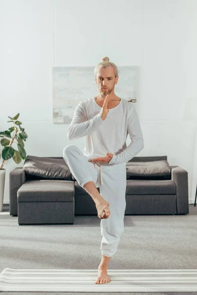 Sporty adult man balancing in yoga pose on mat at home — Stock Photo