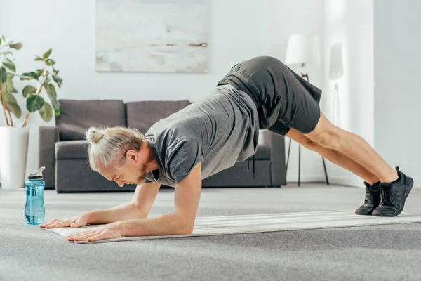 Vista laterale di atletico uomo adulto in abbigliamento sportivo esercizio su tappetino yoga a casa — Foto stock