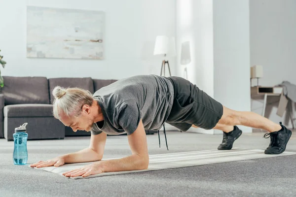Спортсмен в спортивной одежде делает упражнения на доске на коврике для йоги дома — стоковое фото