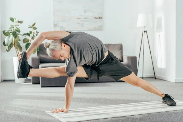 Спортивный взрослый мужчина в спортивной одежде, растянувшийся на коврике для йоги дома — стоковое фото