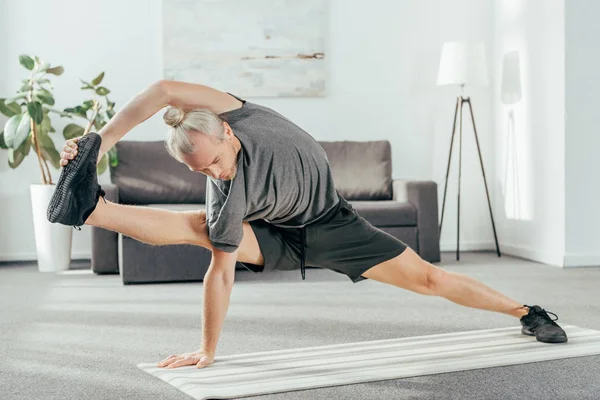 Deportista adulto hombre equilibrio y estiramiento en yoga mat en casa - foto de stock