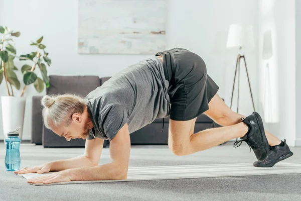 Side view of athletic man in sportswear training on yoga mat at home — Stock Photo