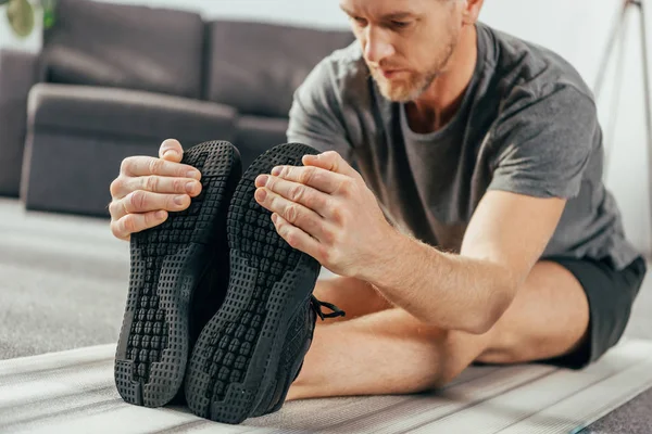 Tiro recortado de hombre atlético en ropa deportiva ejercitando y estirando en la esterilla de yoga en casa - foto de stock