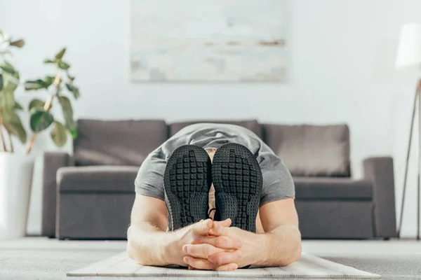 Крупним планом вид на ноги в спортивному взутті дорослого чоловіка займається і розтягується на йога килимок вдома — стокове фото