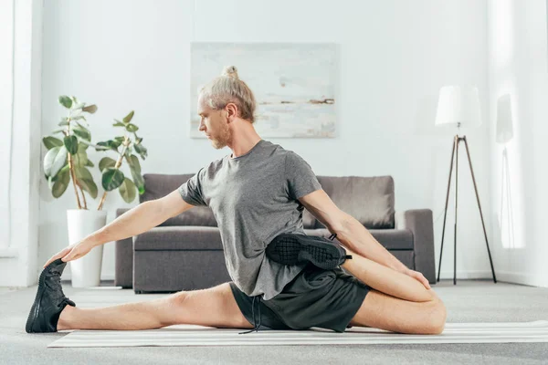 Handsome adult man stretching on yoga mat while exercising at home — Stock Photo