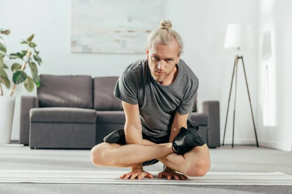Дорослий чоловік балансує на руках з схрещеними ногами і дивиться на камеру під час тренувань вдома — стокове фото