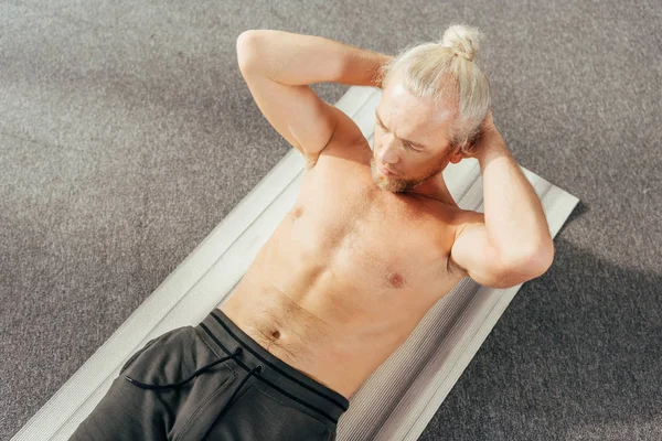 Высокий угол зрения человек без рубашки делать упражнения ABS на коврик для йоги у себя дома — стоковое фото