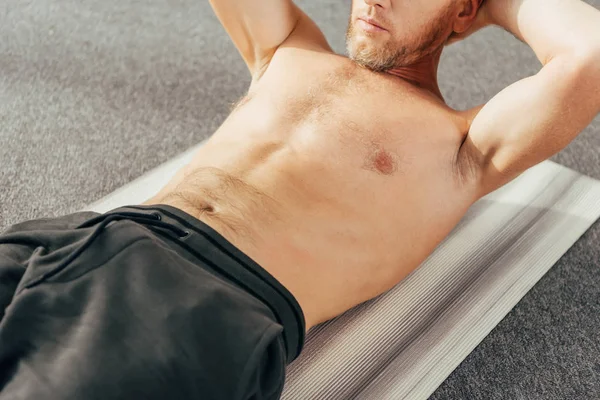 Cropped shot of shirtless man doing abs exercise on yoga mat at home — Stock Photo