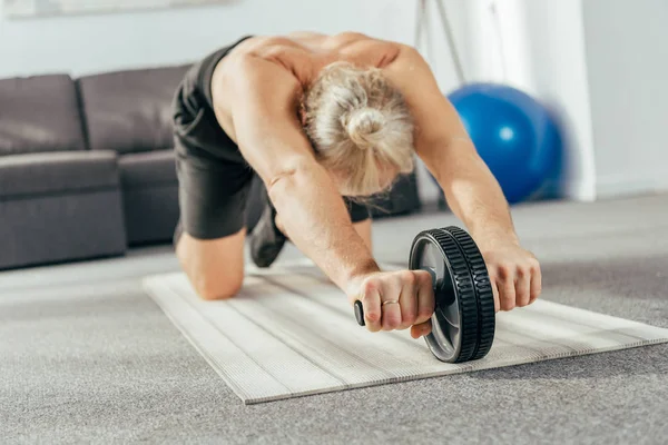 Muscular adult man exercising with abs wheel at home — Stock Photo