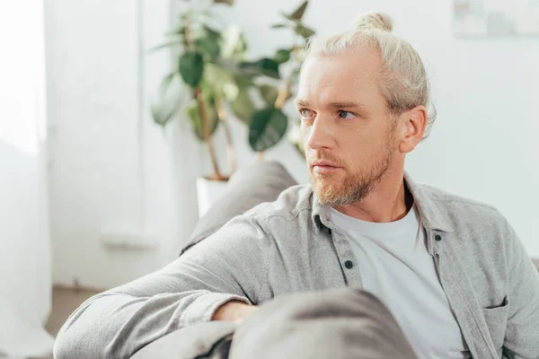 Bel homme adulte assis sur le canapé et regardant loin — Photo de stock