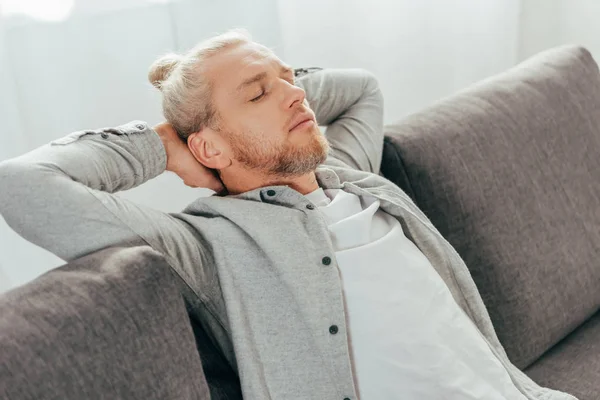 Homem adulto bonito dormindo com as mãos atrás da cabeça no sofá — Fotografia de Stock