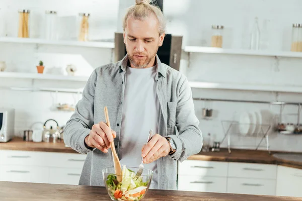 Handsome adult man cooking vegetable salad at home — Stock Photo