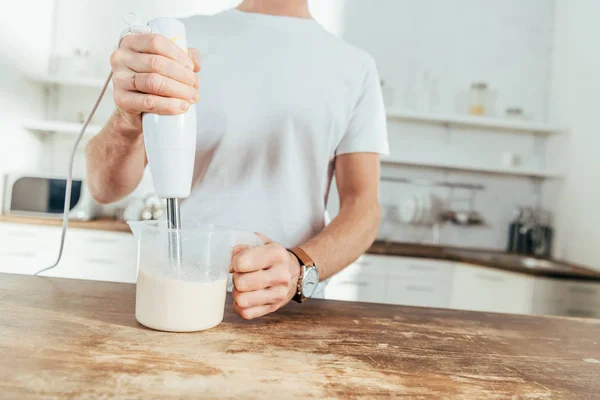 Tiro recortado de hombre mezclando batido de proteínas con licuadora eléctrica en casa - foto de stock