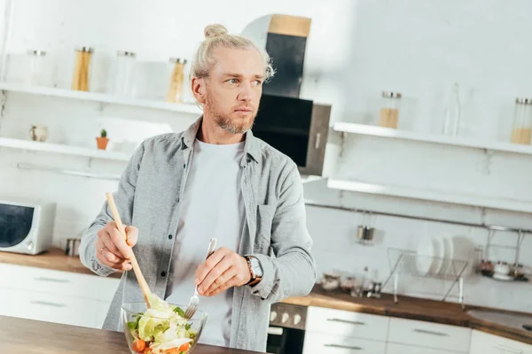 Взрослый мужчина готовит овощной салат и смотрит в сторону на кухне — стоковое фото