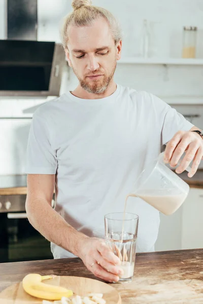 Uomo adulto versando banana frullato proteico in vetro a casa — Foto stock