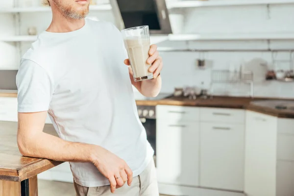 Tiro recortado de hombre deportivo sosteniendo vidrio con batido de proteínas en casa - foto de stock