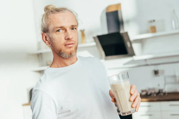 Sportlicher Mann hält Glas mit Proteinshake und blickt in die Kamera — Stockfoto