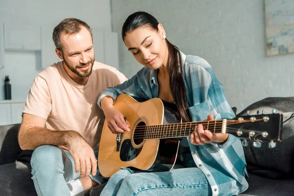Bonito marido ensinando bela esposa para jogar guitarra acústica — Fotografia de Stock