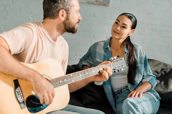 Guapo marido tocando la guitarra acústica mientras hermosa esposa escuchándolo - foto de stock