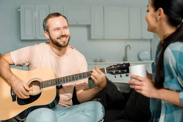 Mari souriant jouant de la guitare acoustique tout en écoutant femme — Photo de stock