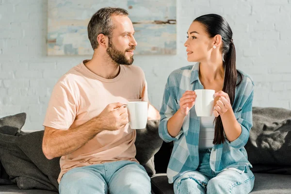 Чоловік і дружина сидять на дивані, п'ють каву і дивляться один на одного — стокове фото