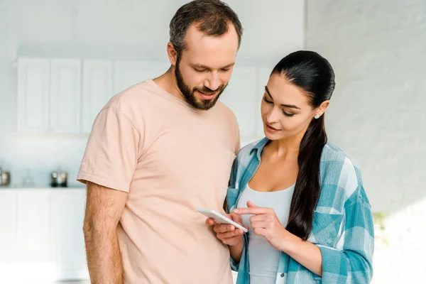 Hermosa pareja en ropa casual usando teléfono inteligente en casa - foto de stock